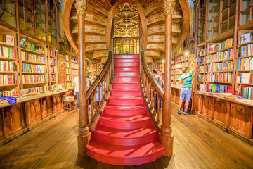 Fototapeta premium Oporto, Portugal - August 13, 2017: large wooden staircase with red steps inside Library Lello and Irmao in historic center of Porto, famous for Harry Potter film. Horizontal shot.