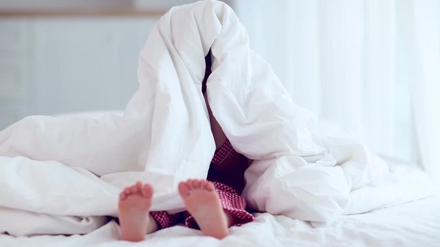 cute happy little boy, kid playing peekaboo, hiding under the blanket on the bed