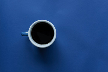 Cup of coffee on blue paper background, dark blue tones image for background, minimalist photo