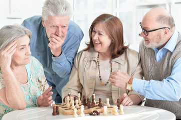 Close up portrait of two senior couples sitting at table and playing chess