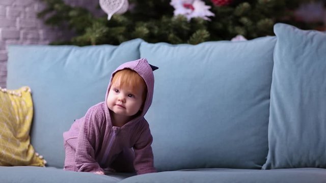 cute little baby in purple dinosaur romper crawling on sofa at home on christmas time