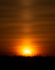 Dramatic sunrise colors as intense yellow sun ball rises over a silhouetted ridge creating an orange streaked sky.