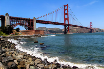 Naklejka premium USA San Francisco June 2018: Photo of the attractions of the Golden Gate Bridge near the water with waves and stones