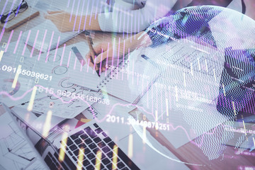 A woman hands writing information about stock market in notepad. Forex chart holograms in front. Concept of research. Double exposure