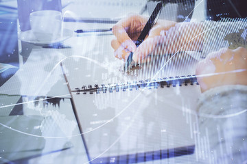 Hand taking notes in notepad. Forex chart holograms in front. Concept of research. Double exposure