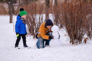 Fototapeta na wymiar Happy family with kid having fun and playing with snow outdoors in winter nature. Man, father and child boy on Christmas holidays walking in a snowy park, making snowman. Wintertime vacation.