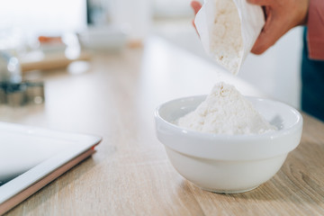 Woman Hands adding Flour to Bowl on White Wooden Background to Make Cake.