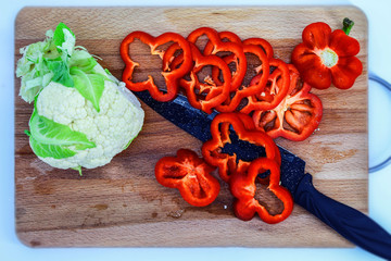 Sliced rings of red bell pepper and cauliflower lie on a wooden Board for cutting and slicing products, among the vegetables ceramic knife