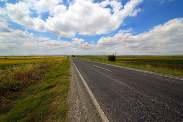 A country road along with a beautiful sky and fields.
