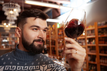 Close up of a cheerful bearded man tasting red wine at wine store. Attractive man shopping at the supermarket, choosing red wine