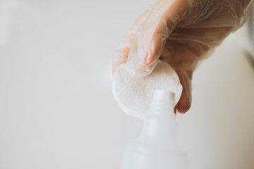 Womans manicurist hand in medical gloves. holding a bottle with lotion or acetone, apllying on cotton pad