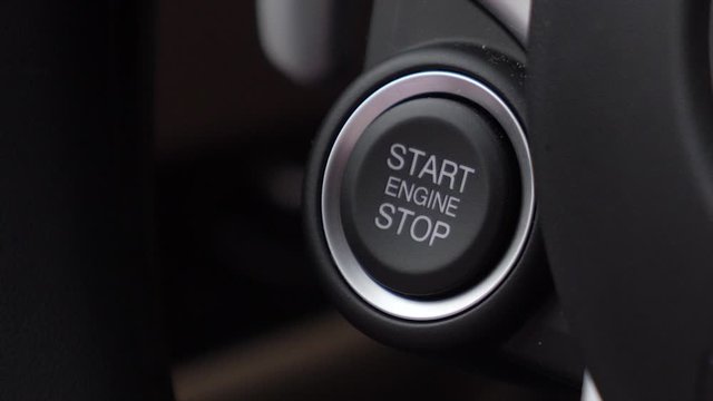 A close up shot of a person starting the engine of a car on the start button