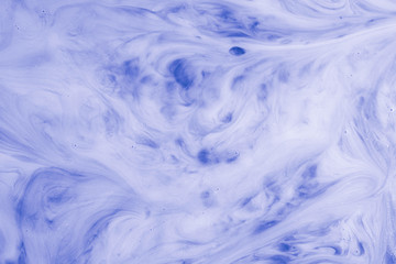 A macro photo of drops of blue food dye swirled and mixed into thick creamy white milk to give a...