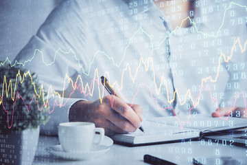 Double exposure of man's hands writing notes of stock market with forex chart.