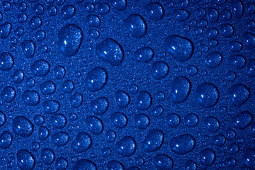 A close up abstract macro photo of water droplets on a grey non stick frying pan material lit with a blue flash gel