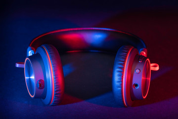 A pair of generic headphones made of brushed metal with a leather headband lit with a red and blue flash gels