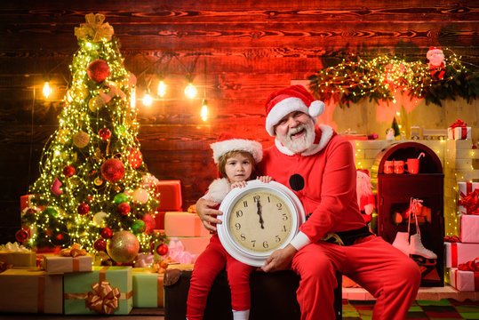New year midnight. Merry Christmas. Kid boy dressed as Santa Claus is waiting for Christmas. Christmas boy with clock. Little assistant holds old clock. Time for christmas. Happy New Year. Santa man.