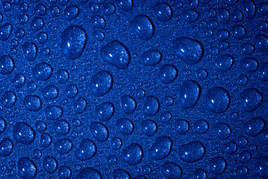 A close up abstract macro photo of water droplets on a grey non stick frying pan material lit with a blue flash gel