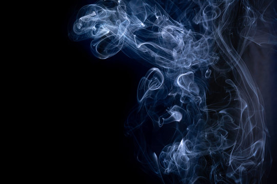 A close up macro photo of incense smoke lit by a blue flash to create a moody glow overlay with copy space