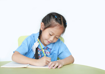 Naklejka premium Happy little schoolgirl writing on notebook at desk isolated on white background. Children and Education concept.