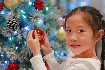 Portrait of happy Asian little girl holding christmas ball of christmas tree in the winter season and happy new year festival.
