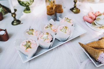 Tasty birthday cupcakes of pink pastel color with stars on top, waiting on the table among other confections. Festive composition.