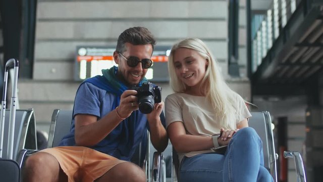 Happy couple sitting in departure lounge with baggage and photo camera in airport
