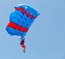 Paratrooper in red suit descends under canopy of parachute