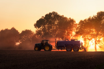 Tractor fertilizing agricultural field at sunset. Agriculture