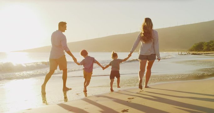 Happy family skipping on the beach holding hands together at sunset, two toddler boys holding hands with their mom and dad enjoying the beach, amazing family vacation