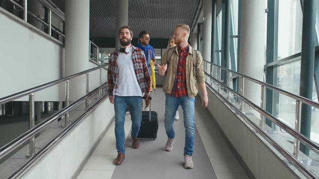 Full length of four friends with baggage walking through airport and communicating