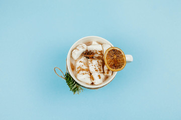 A large white mug with cocoa and marshmallows, cinnamon on a blue background. Christmas motives. Traditional winter drink.