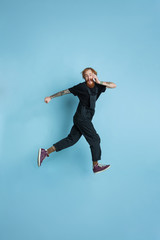 Obraz premium Portrait of young caucasian man looks dreamful, cute and happy. Jumping. laughting on blue studio background. Copyspace for your advertising. Concept of future, target, dreams, visualisation.