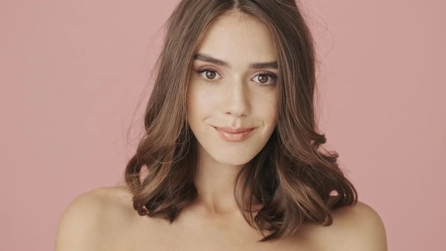 Beautiful calm half-naked woman is opening her eyes isolated over pink background
