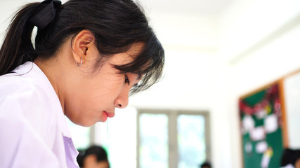 Girl Asian student concentrate one's mind writing test in exam on paper answer sheet, serious...