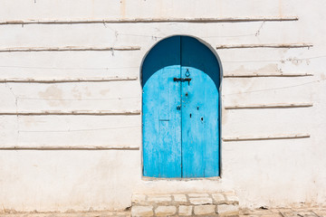 Rustic wall and old wooden blue door. Traditional rural house facade in Tunisia