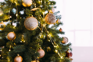 Obraz na płótnie Canvas Close-up Christmas tree with beautiful golden Christmas tree decorations on Christmas Eve by the window