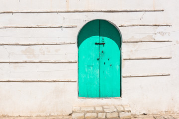 Rustic wall and old wooden green door. Traditional rural house facade in Tunisia