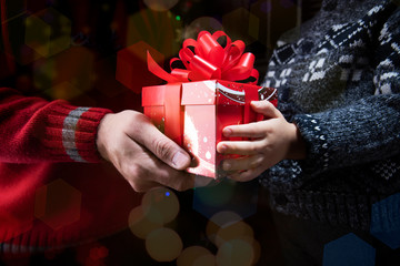 Man gives a gift to a child. Hands with a gift box close-up on the festive bokeh background
