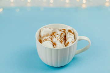 A large white mug with cocoa and marshmallows, cinnamon on a blue background. Christmas motives. Traditional winter drink.