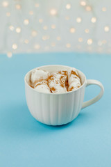 A large white mug with cocoa and marshmallows, cinnamon on a blue background. Christmas motives. Traditional winter drink.