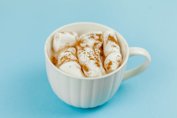 A large white mug with cocoa and marshmallows, cinnamon on a blue background. Christmas motives. Traditional winter drink.