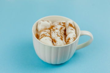 A large white mug with cocoa and marshmallows, cinnamon on a blue background. Christmas motives. Traditional winter drink.