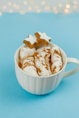 A large white mug with cocoa and marshmallows, cinnamon on a blue background. Christmas cookies. Traditional winter drink.