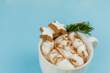 A large white mug with cocoa and marshmallows, cinnamon on a blue background. Christmas cookies. Traditional winter drink.
