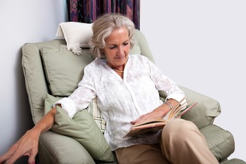 Senior woman reading book while relaxing on armchair at home