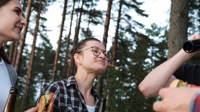 A group of friends rests and relaxes in nature. People eat hamburgers, drink beer, communicate and laugh. The concept of a weekend in the forest.