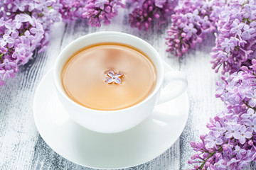 Cup of herbal tea and lilac on wooden background. Rays of sunlight