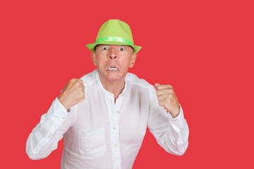 Portrait of an angry senior man clenching fists against red background