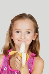 Portrait of young girl holding banana against gray background